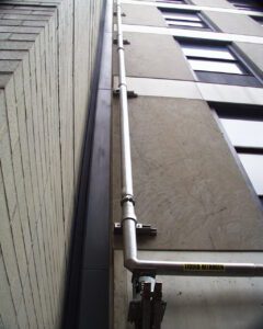 A metal pipe clamped to a building and going upwords