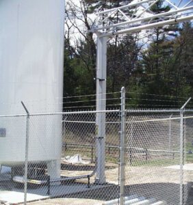 A large silver metal tank with wire fence around it with trees in background